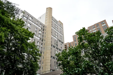 The Landings residential tower seen through leafy trees with nearby apartment buildings.